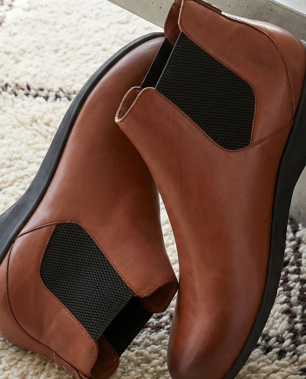 Brown leather ankle boots on a textured rug with a modern interior setting.